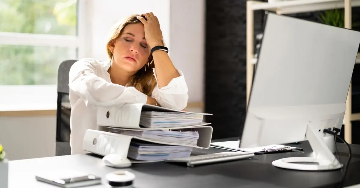 businesswoman at desk showing physical signs of workplace stress